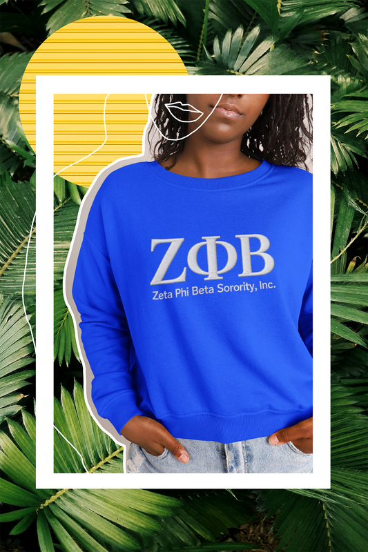 Person wearing a blue sweatshirt with Zeta Phi Beta Sorority, Inc. logo against a tropical leaf background